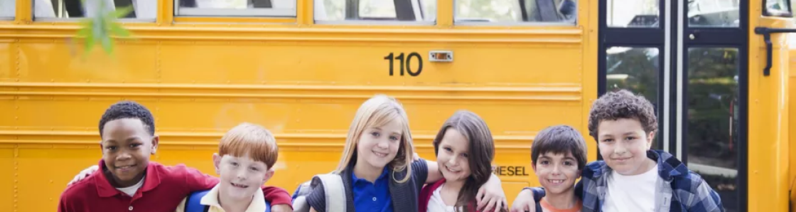 Crianças abraçadas em pose pra foto em frente à um ônibus escolar